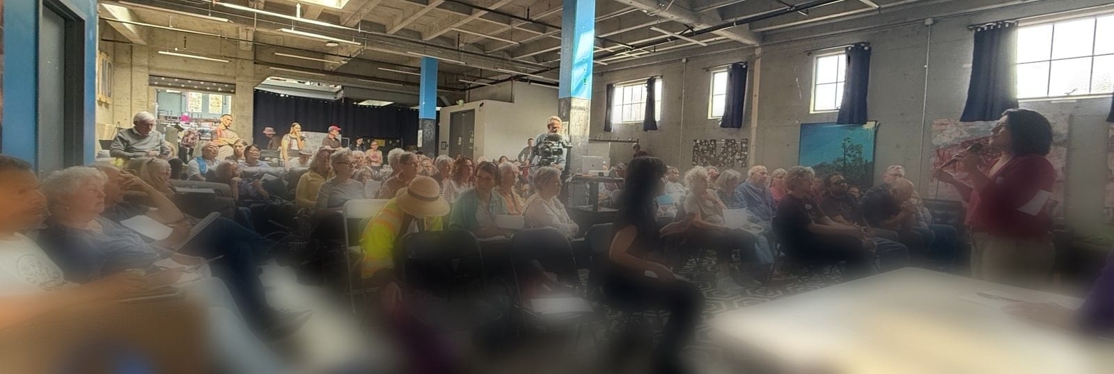 A full community room at the August 16th candidate forum, with residents seated in rows and a speaker addressing them.